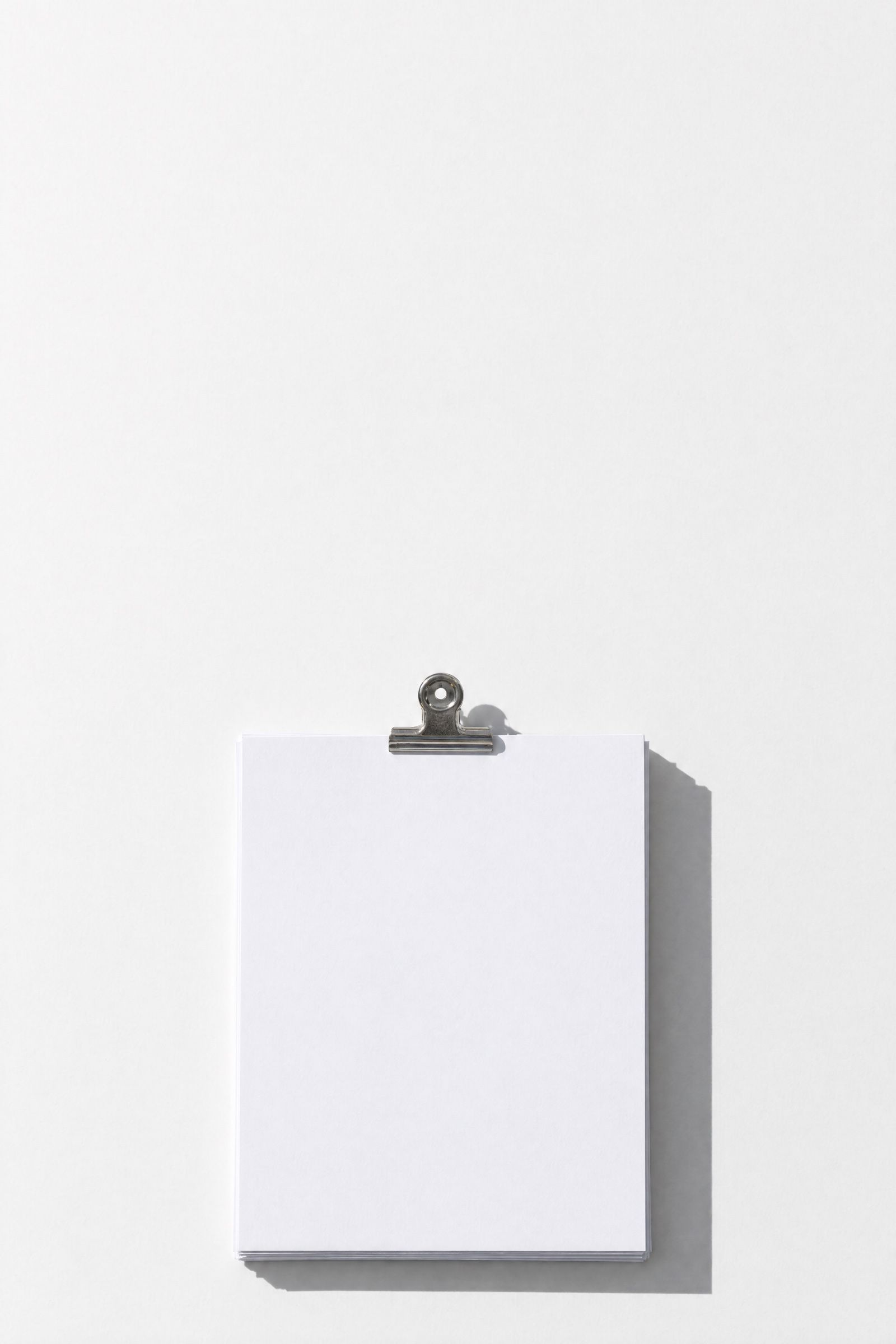 A squared stack of blank white invoices held by one steel bulldog clip, casting a long shadow.